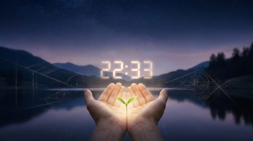 Mains ouvertes tenant une jeune pousse devant un lac au crépuscule affichant l'heure numérique 22h33.