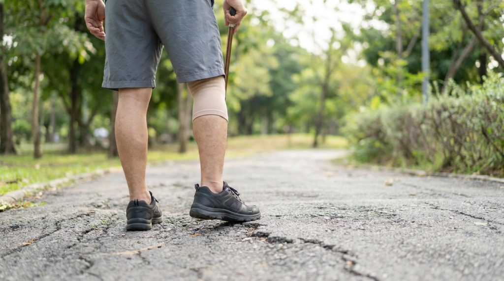 Personne marchant avec une canne et une genouillère sur un chemin en extérieur.