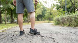 Personne marchant avec une canne et une genouillère sur un chemin en extérieur.