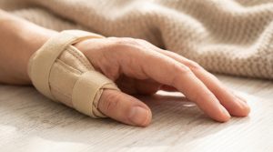 Main portant une orthèse beige pour immobiliser le pouce sur un fond en bois.